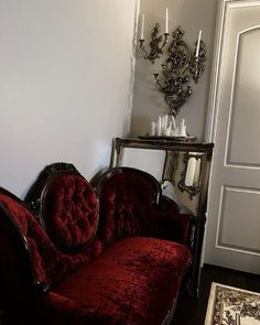 a red couch sitting in the corner of a living room next to a mirror and chandelier