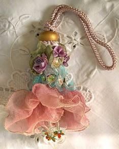 a pink purse with flowers on it sitting on a white lace tablecloth, next to a beaded necklace