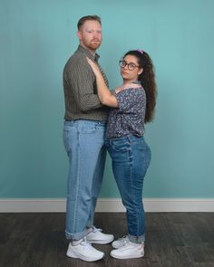 a man and woman standing next to each other in front of a blue wall with their arms around each other