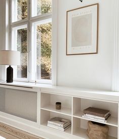 there is a white shelf with books on it and a lamp next to the window