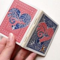 a hand holding two playing cards in it's left hand, both with red and blue designs on them