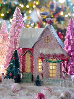 a christmas scene with a house and trees in the snow, lights are on behind it