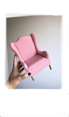 a hand holding up a pink chair with nails on it