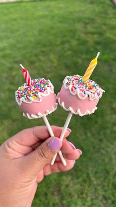 two pink cake pops with sprinkles and candles are held in front of the camera