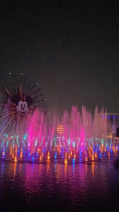 colorful lights and water show at night with mickey mouse in the center surrounded by buildings