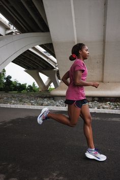 a woman running on the road under a bridge with her head turned to the side