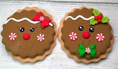 two decorated cookies sitting on top of a white wooden table with red and green bows