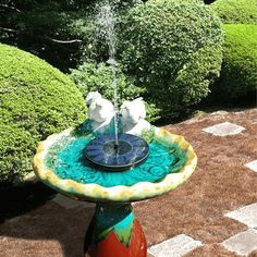 there is a fountain in the middle of some bushes and grass with two white swans on it