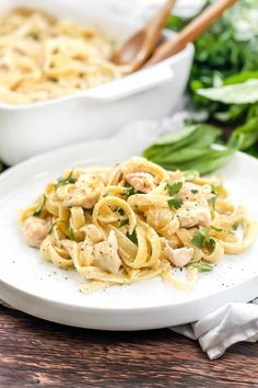 a plate of pasta with chicken and parsley on it next to a bowl of spinach