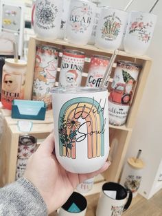 a person holding up a coffee cup in front of many mugs on the shelves