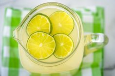 three lemons in a pitcher filled with water on a green and white checkered tablecloth