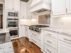 a kitchen with white cabinets and marble counter tops, wood flooring and stainless steel appliances