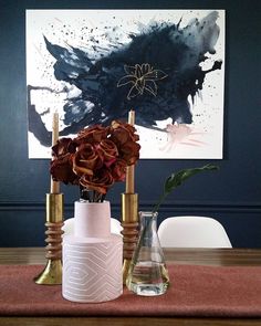 two vases with flowers in them sitting on a wooden table next to a painting