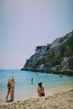 people are sitting on the beach and swimming in the water, while one person is wearing a bathing suit