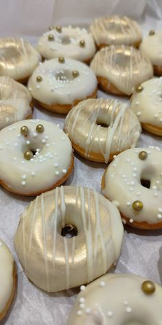 there are many donuts with white frosting and gold sprinkles on them