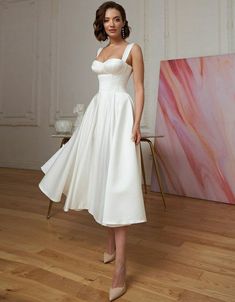 a woman in a white dress standing on a hard wood floor next to a painting