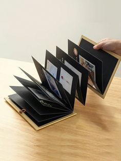 a person holding an open folder with photos inside it on a table top next to a hand