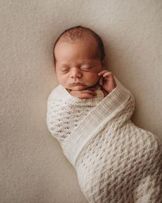 a newborn baby is wrapped in a white blanket and sleeping on his side with his hands under his chin