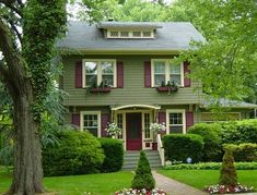 a green house with red shutters on the front door and two trees in front