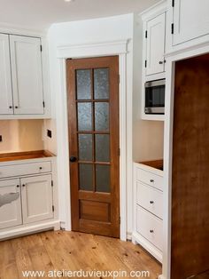 an empty kitchen with white cabinets and wood flooring is pictured in this image, there is a microwave on the cabinet door