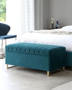 a bed with a blue footstool in front of it and a white bedspread