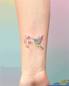 a small hummingbird tattoo on the left side of the arm, with purple flowers and leaves around it