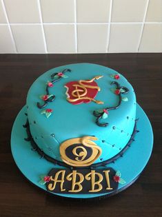 there is a blue cake with gold decorations on it and the name abdi written in gold