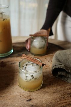 two jars filled with drinks sitting on top of a wooden table next to a person