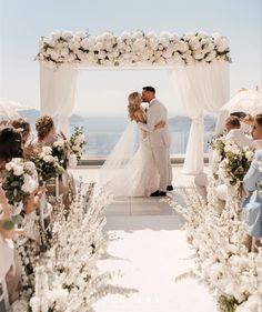 a bride and groom are kissing under an arch with white flowers