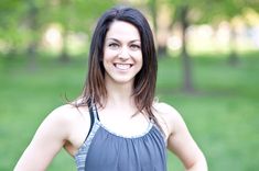 a woman standing in the grass with her hands on her hips and smiling at the camera