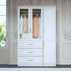 a white closet with clothes hanging on it's doors and drawers in front of a window