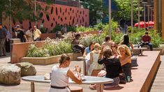 people are sitting at tables in the middle of an outdoor area with plants and trees