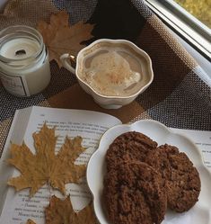 two cookies are on a plate next to a cup of coffee and an open book