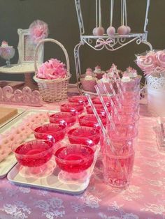 a table topped with lots of pink cups and trays filled with desserts on top of it