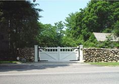 a stone wall and gate in front of a house with trees on the other side