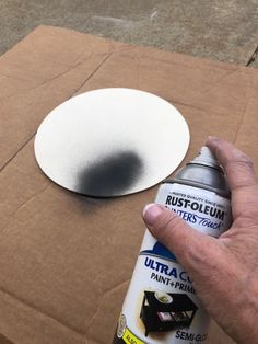 a hand is holding a spray bottle next to a cardboard box with a hole in it