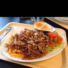 a white plate topped with lots of food on top of a wooden tray next to silverware