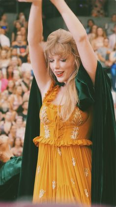 a woman in a yellow dress is holding her arms above her head and looking at the crowd