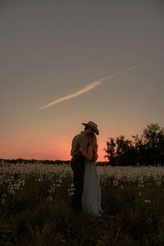 a man and woman standing in a field at sunset