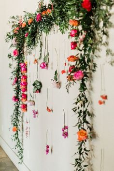 an arrangement of flowers and greenery is hanging on the side of a white wall