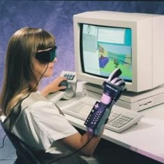 a woman sitting in front of a computer with a glove on her arm holding a cell phone