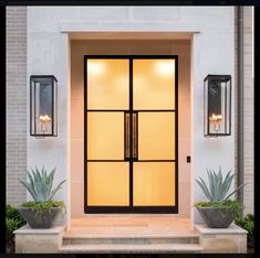 an entrance with two planters and one light on the side of the door that is lit up