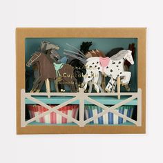 wooden toy horses are on display in a cardboard box with blue and white striped ribbon