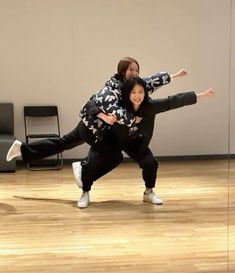 two people in black and white outfits are dancing on a wooden floor with chairs behind them