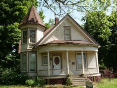 a white house with a brown roof in the middle of some trees and bushes on either side of it