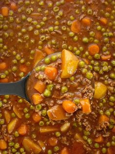 a ladle full of soup with peas and carrots