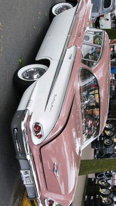 an old pink and white car parked next to other cars