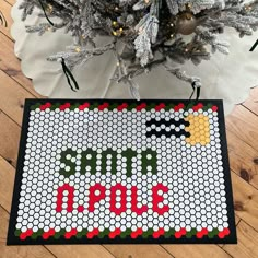 a cross stitch christmas tree ornament on a wood floor next to a decorated christmas tree