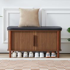 a wooden cabinet with shoes on it in front of a white wall and potted plant