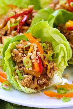 two lettuce wraps filled with meat and vegetables on a white plate next to sliced carrots